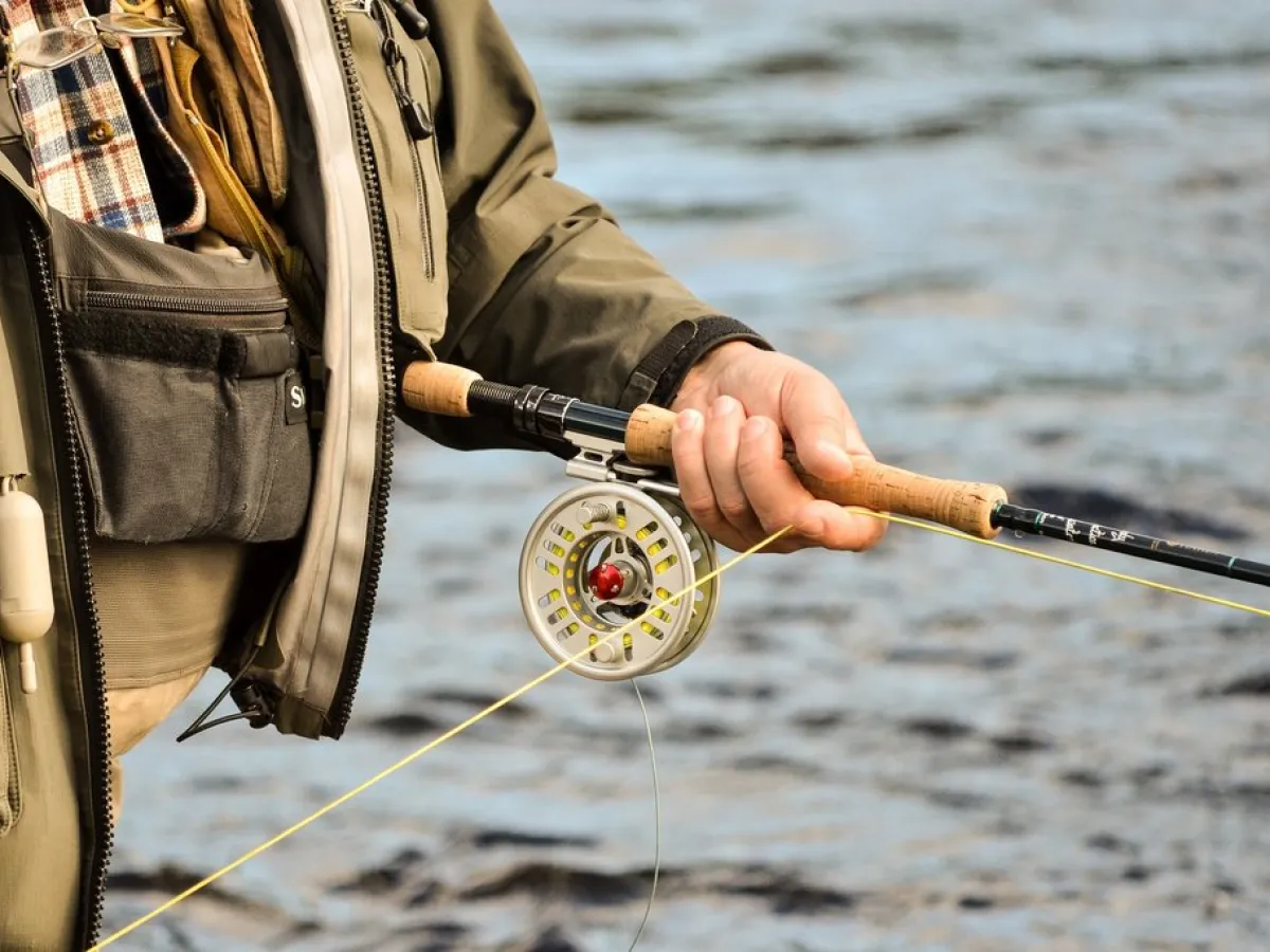 Person holding a fly fishing rod & reel near water