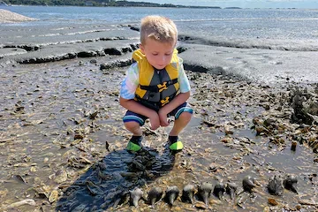 a young boy standing next to a body of water